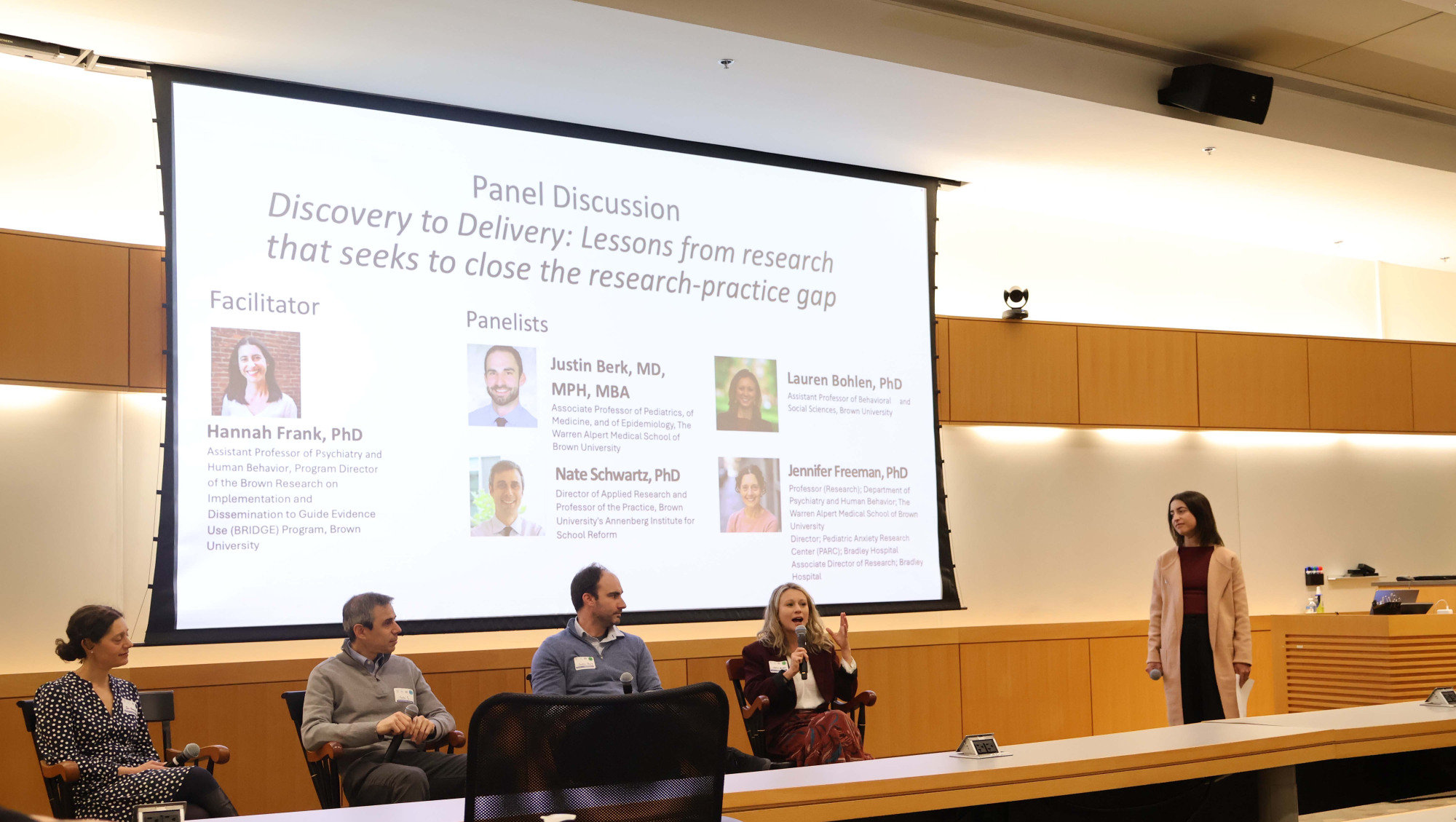 4 panelists (two women and two men) sit facing Dr. Hannah Frank, who is moderating.