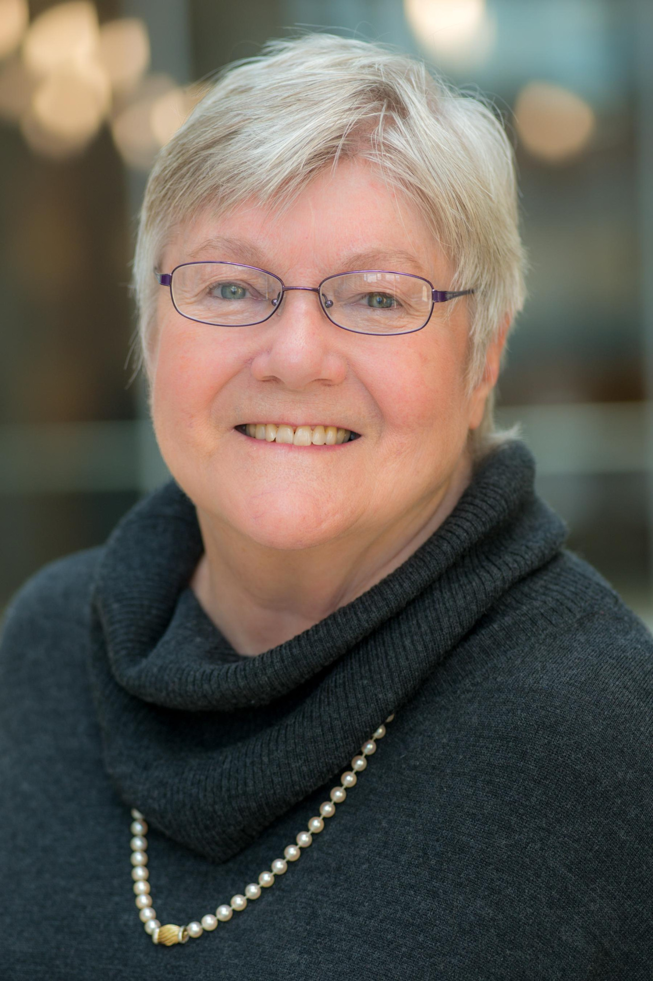 Portrait of Dr. Sharon Rounds, a woman with short gray hair wearing a dark gray sweater and long pearl necklace.